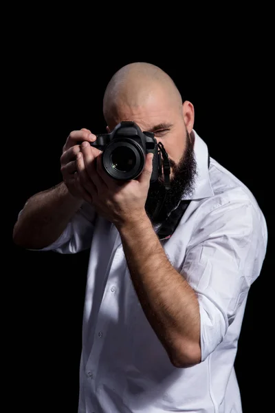 Фотограф з фотоапаратом. Чоловічий фотограф з бородою в білій сорочці бере фотон на чорному тлі — стокове фото