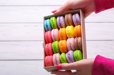 Hediye kutusu beyaz ahşap arka plan arka plan, üstten görünüm üzerinde lezzetli macaroons ile holding eller.