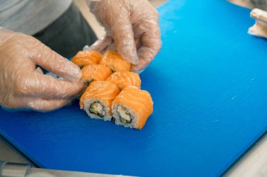 Şef koyarak suşi eller. Yemek lezzetli suşi rulo siyah plaka üzerine yerleştirerek eldiven.
