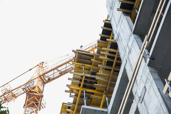 A building crane, stands near an unfinished building, a view from below. Construction crane