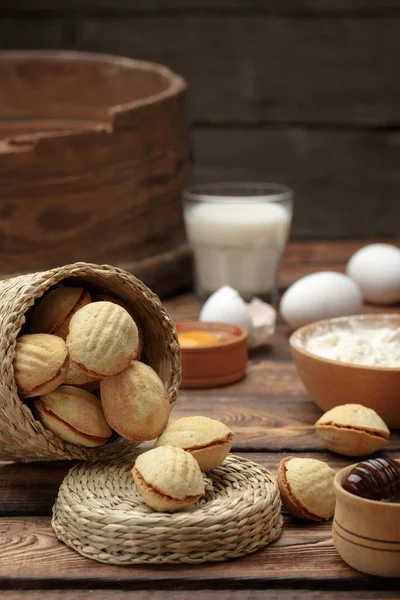 Heerlijke walnoot vormige zandkoekkoekjes broodje gevuld met zoete gecondenseerde melk en gehakte pistachenoten. tegen de achtergrond van de ingrediënten, weergave van bovenaf, close-up — Stockfoto