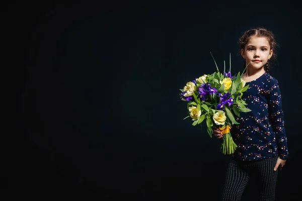 Liten flicka med blombukett i handen. Begreppet lycka, människor, barn, barndom. Studio foto på en svart bakgrund. utrymme för text — Stockfoto