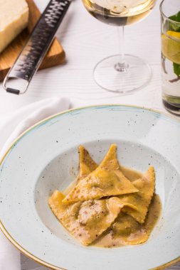 Plaka üzerinde fesleğen ve parmesan peynirli mantı makarna. Bir kesme tahtası üzerinde rende parmesan. dikey fotoğraf