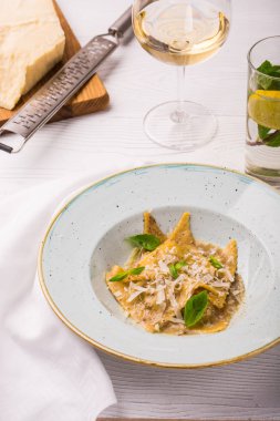 Plaka üzerinde fesleğen ve parmesan peynirli mantı makarna. Bir kesme tahtası üzerinde rende parmesan. dikey fotoğraf