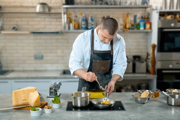 Chef in apron stirring ravioli pasta in frying pan on burner in restaurant kitchen — Stock Photo, Image