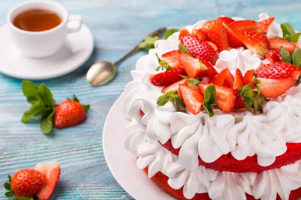 beautiful cake with strawberries and cream with tea ob blue wooden background