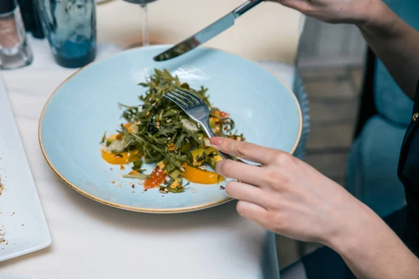 Female eating restaurant dish with fork and knife on plate on table at the restaurants. Salad with spinach, arugula, cheese, orange