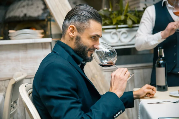 Bonito barbudo rico homem com bigode elegante e barba segurando vidro e cheirar o cheiro de vinho tinto no restaurador . — Fotografia de Stock