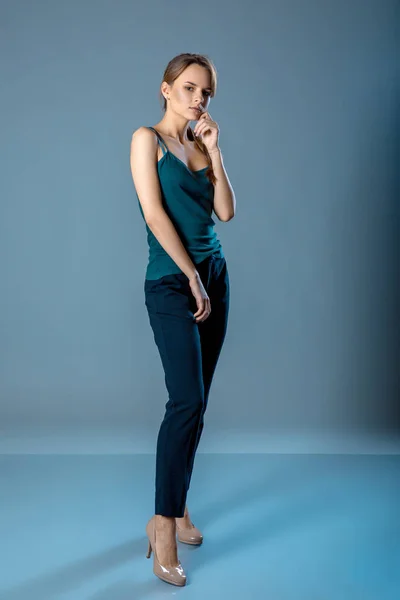 Full längd porträtt av ung kvinna i mörk grön skjorta och mörka byxor stående på en blå grå bakgrund. — Stockfoto