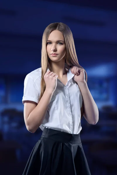 Uma adolescente bonita a olhar para ti com confiança contra um passado de escola desfocada. a menina está vestida com uniforme escolar blusa branca e saia preta — Fotografia de Stock