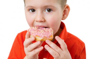 Küçük mutlu sevimli çocuk beyaz arka plan duvar üzerinde donut yiyor. Çocuk eğlenceli poğaça ile geçiriyor. Çocuklar için lezzetli yemekler. Komik zaman evde yiyecek ile. Parlak çocuk.