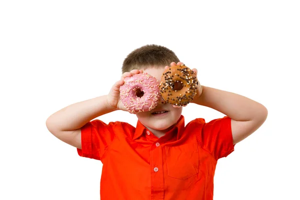 Peuter babyjongen met twee turquoise donuts op zijn ogen op witte achtergrond muur. Kind is het hebben van pret en kijkt door donut. Lekker eten voor kinderen. Grappige tijd thuis met zoete voedsel. — Stockfoto