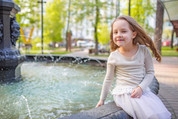 Söt liten flicka spelar vid staden fontänen på varm och solig sommardag. Barnet har roligt med vatten på sommaren. Aktiv fritid för barn. — Stockfoto