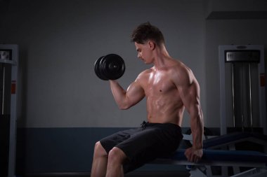 Pazı, stüdyoda karanlık bir arka plan üzerinde için egzersizleri yapıyor şort, yakışıklı genç adam