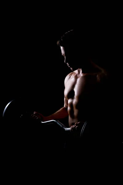 Primer plano del joven musculoso levantando pesas sobre fondo oscuro —  Fotos de Stock