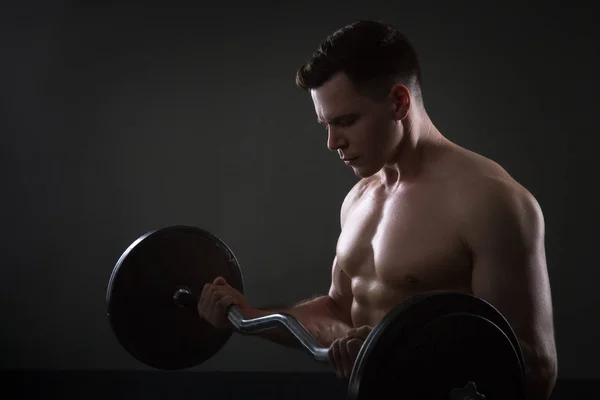 Primer plano del joven musculoso levantando pesas sobre fondo oscuro —  Fotos de Stock