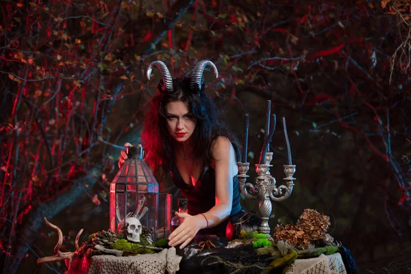 Beautiful witch with horns on her head is being prepared to make the witchcraft over the forest background. Halloween image. — Stock Photo, Image