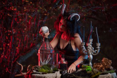 Kafasında boynuzları olan güzel bir cadı cadılar bayramı kutlaması için insan kafatasına kara büyü yapıyor. Cadı Cadılar Bayramı kostümü.