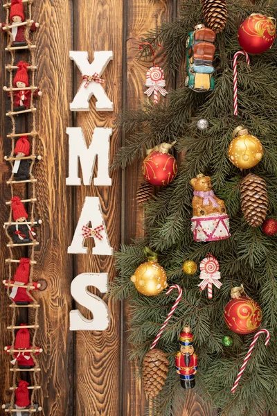 Noel ağacının dalları, kırmızı bebeklerden oluşan bir çelenk ve tahta bir arka planda Noel oyuncakları olan bir Noel arkaplanı. — Stok fotoğraf