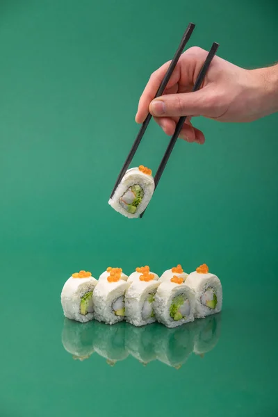 Hand holding sushi roll with chopsticks on green background. set of rolls — Stock Photo, Image