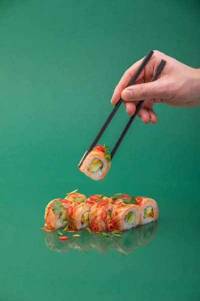 Ręczne trzymanie rolki sushi z pałeczkami na zielonym tle. zestaw rolek — Zdjęcie stockowe