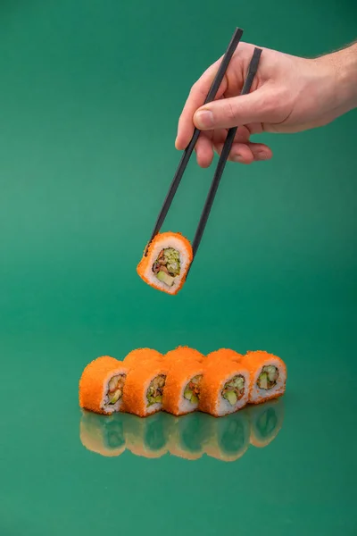 Hand holding sushi roll with chopsticks on green background. set of rolls — ストック写真