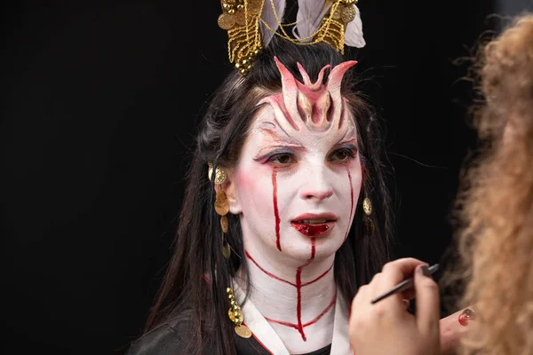 Witchcraft Asian woman in scary Witch ghost story look, mouth blood wound black long hair, studio lighting dark red background. makeup artist doing makeup for halloween