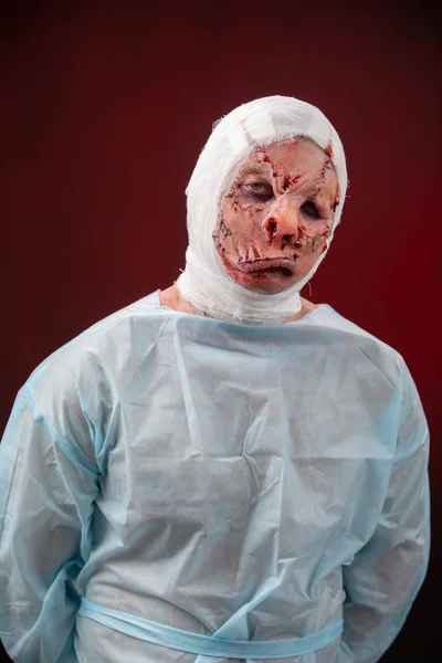 Crazy zombie horror make up. Person in blue madical shirt and bandaged head. Scars, deep scratches realistic art make-up. head is re-banded bandage, beaten with a stick. banner for Halloween party