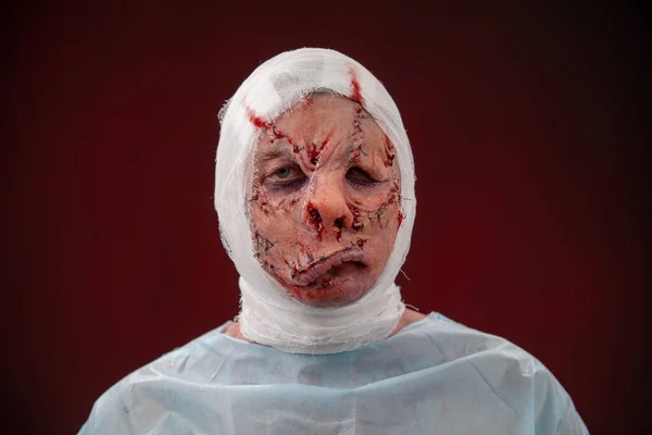 Crazy zombie horror make up. Person in blue madical shirt and bandaged head. Scars, deep scratches realistic art make-up. head is re-banded bandage, beaten with a stick. banner for Halloween party