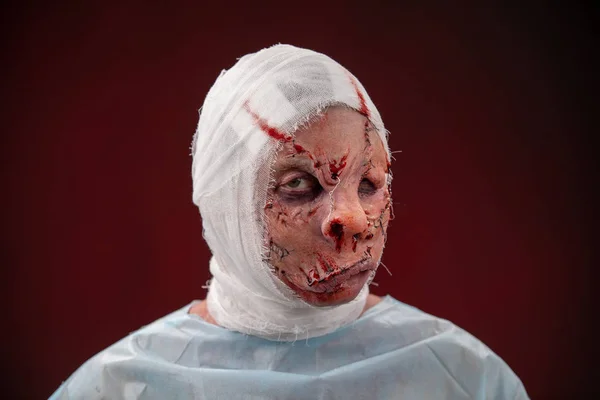 Crazy zombie horror make up. Person in blue madical shirt and bandaged head. Scars, deep scratches realistic art make-up. head is re-banded bandage, beaten with a stick. banner for Halloween party