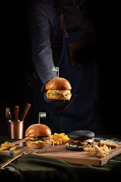 Three Delicious Hamburgers Wooden Board Hand Out Dark Holds Out — Stock Photo, Image