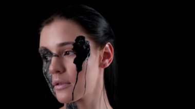 Moda yavaş çekim portresi. Yaratıcı bir makyajı olan model bir kadın. Boyalı karga. Sakin ol cadılar bayramı. Karanlık arka plan. Yüzümden siyah boya akıyor.