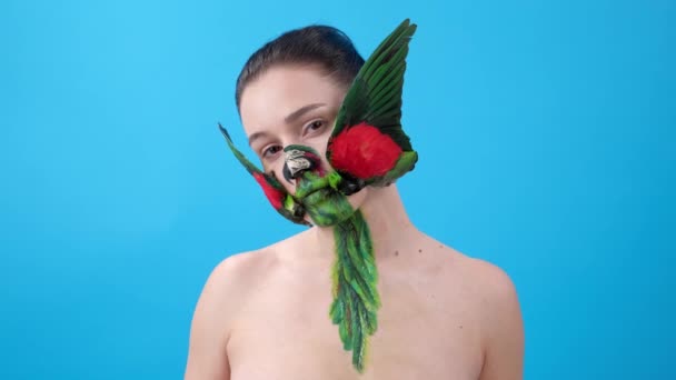 クローズアップ オウムの翼からの化粧を持つ女の子 顔に鳥と体の芸術 青い背景のFemailモデル — ストック動画