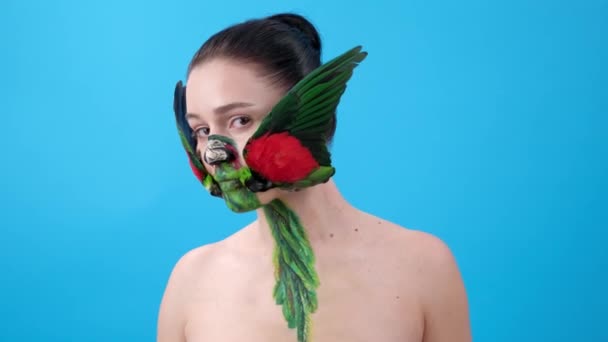 クローズアップ オウムの翼からの化粧を持つ女の子 顔に鳥と体の芸術 青い背景のFemailモデル — ストック動画