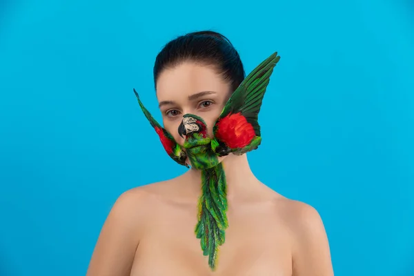 Gyönyörű lány egy papagájmadárral az arcán. fiatal nő színes smink és toll toll szárnyak test művészet — Stock Fotó