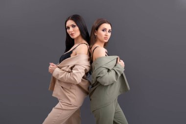 Gri arkaplanda duran takım elbiseli ve üstsüz iki çekici iş kadınının portresi