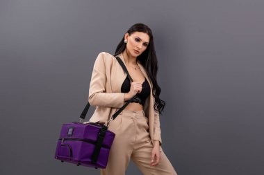 Uzun boylu, çekici, neşeli bir bayan. Büyük bir dava ile yurtdışına seyahat ediyor. Gri arka planda tatil. Stüdyoda takım elbiseli ve üstten poz veren iş kadınının moda portresi.