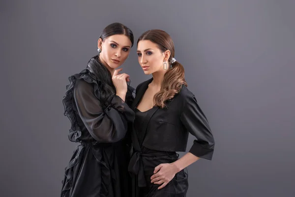 Mode Portrait de deux jolies jeunes femmes dans une robe noire posant sur fond gris . — Photo