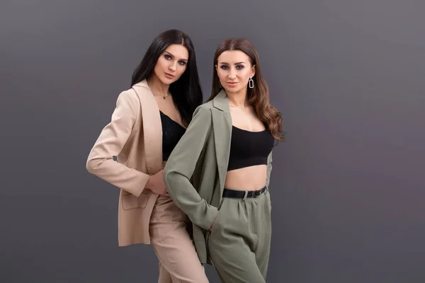 Portrait of Two attractive business women wearing in suits and tops posing on grey background — Stock Photo, Image