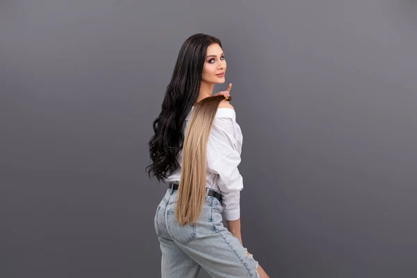 Модный портрет женщины, держащей сечения волос для наращивания на сером фоне — стоковое фото