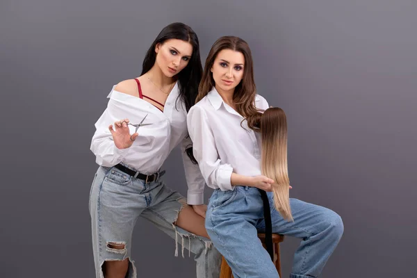 Fashion portrait of two Professional hairdressers. Two hair stylists or artists holding sections of hair for extension or hair tresses and scissors