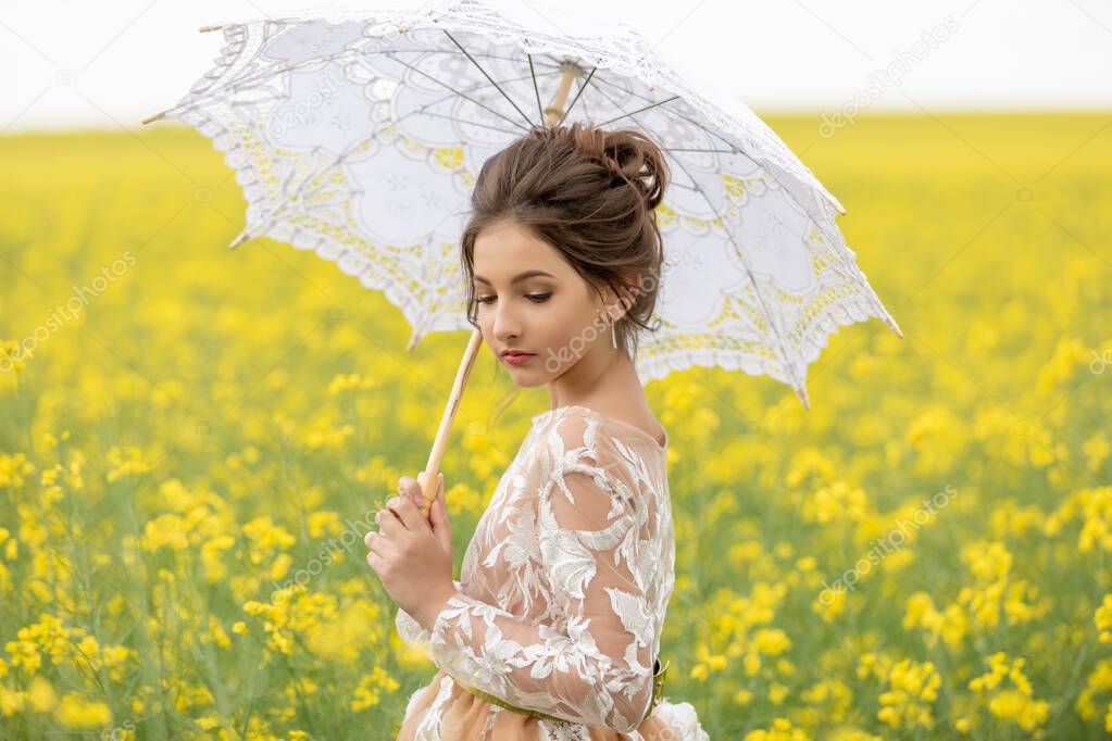 Portrait of young beautiful girl in retro style under a lace umbrella in a field with tall yellow rapeseed flowers. purity and innocence