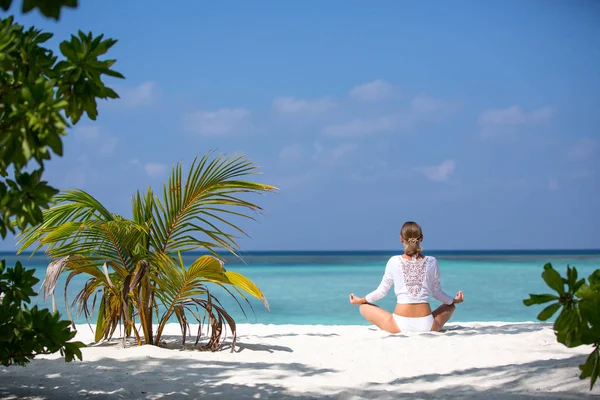 Meditation Yoga woman meditating at serene tropical beach. Girl relaxing in lotus pose in calm zen moment at ocean water. Multiracial girl Slim body tanned model. Health and fitness retreat concept