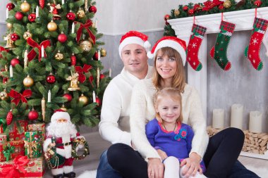 Noel ve yeni yıl kutlama. Mutlu genç aile xmas hediye Noel ağacının yanında oturuyor. Bir şömine arka plan üzerinde Noel çorap ile