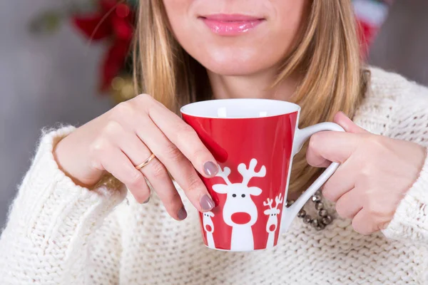 Close up shot of cup in hands of woman with hot drink on Christmas tree background, happy holiday concept — Stock Photo, Image