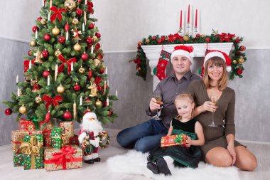 Noel ve yeni yıl kutlama. Üç Kişilik neşeli mutlu aile portresi xmas hediye Noel ağacı yakınındaki ile kutluyor. Bir şömine arkalarındaki Noel çorap ile