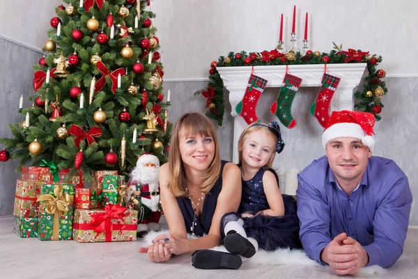 Noel ve yeni yıl kutlama. Üç Kişilik xmas hediye ile Noel ağacı yakın yerde yatan neşeli mutlu aile portresi. Bir şömine arkalarındaki Noel çorap ile