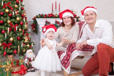 Noel ve yeni yıl kutlama. Üç Kişilik xmas hediye ile Noel ağacı yakınındaki neşeli genç aile portresi. Arka plan üzerinde Noel çorap ile bir şömine. İyi Bayramlar