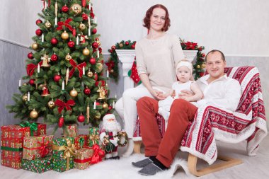 Noel ve yeni yıl kutlama. Üç Kişilik xmas hediye ile Noel ağacı yakınındaki neşeli genç aile portresi. Arka plan üzerinde Noel çorap ile bir şömine. İyi Bayramlar