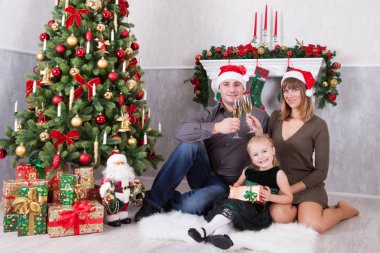Noel ve yeni yıl kutlama. Üç Kişilik neşeli mutlu aile portresi xmas hediye Noel ağacı yakınındaki ile kutluyor. Bir şömine arkalarındaki Noel çorap ile